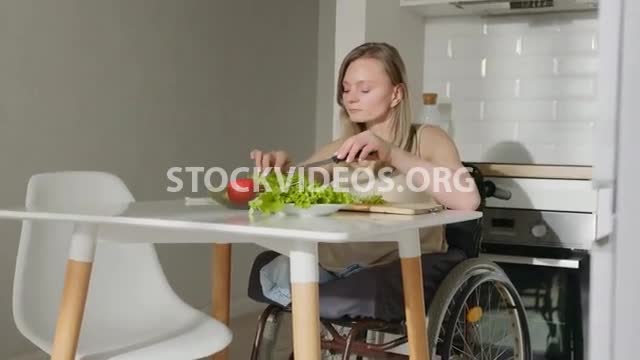 Bilateral amputee woman in wheelchair making salad in kitchen ...